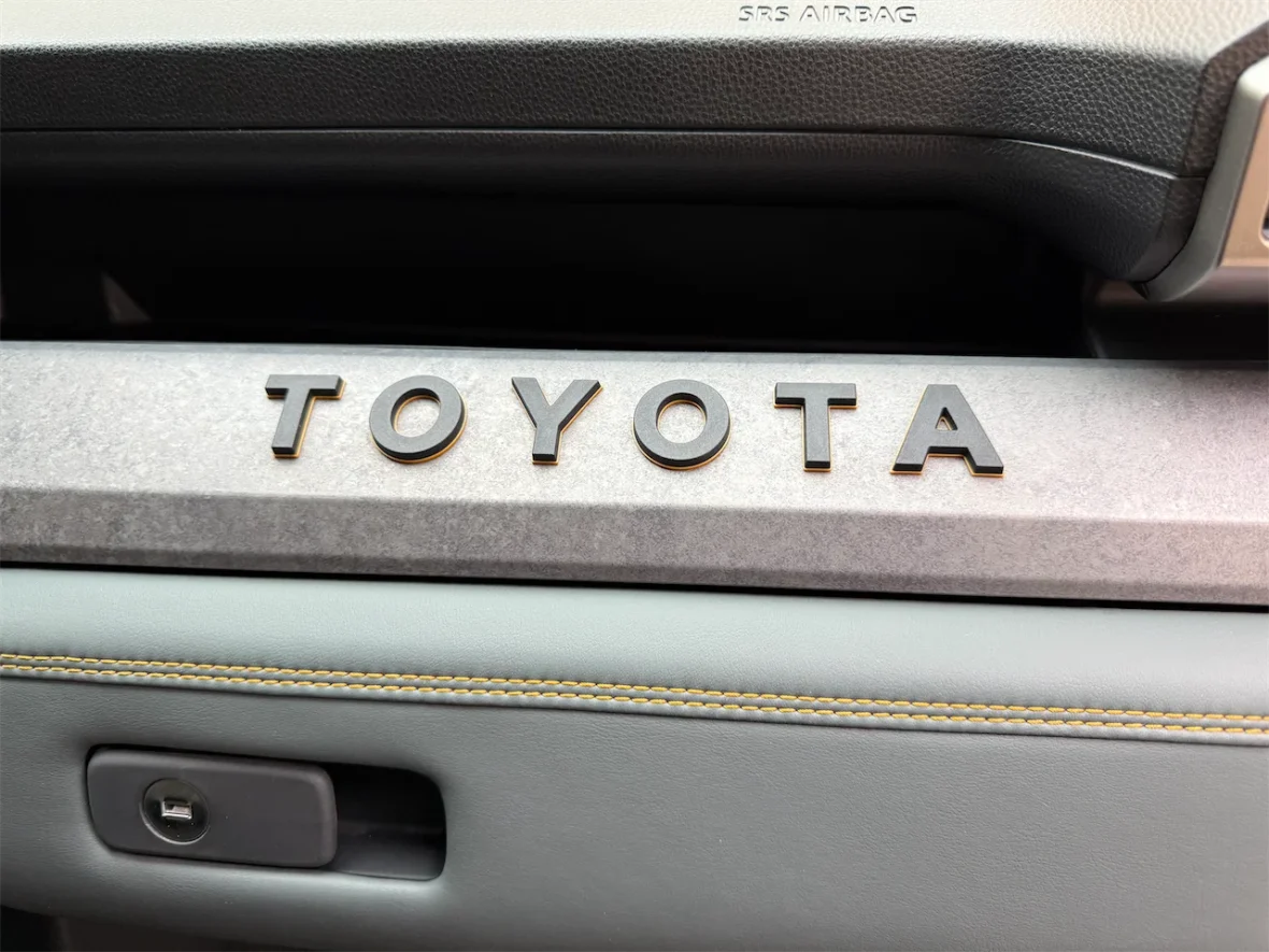 Close-up view of a Toyota logo on the dashboard of a car, featuring sleek design and gray upholstery.