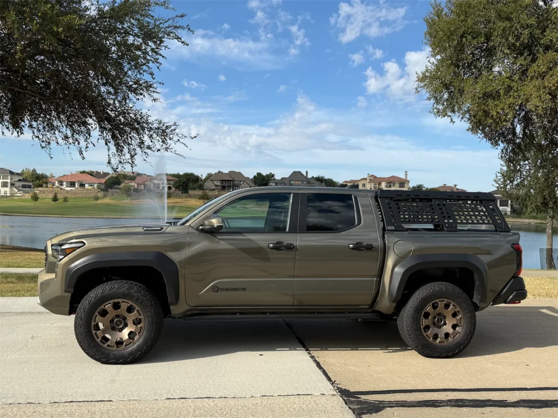 Side view of the 2026 Toyota Tacoma Trailhunter in Bronze Oxide parked beside a lake with an ARB rack in the bed.