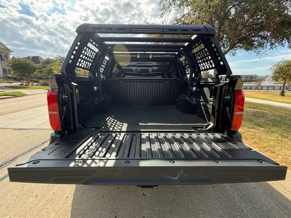 Open truck bed showcasing a spacious interior with a black lined surface and a lattice-style cover, parked on a street with trees and houses in the background.