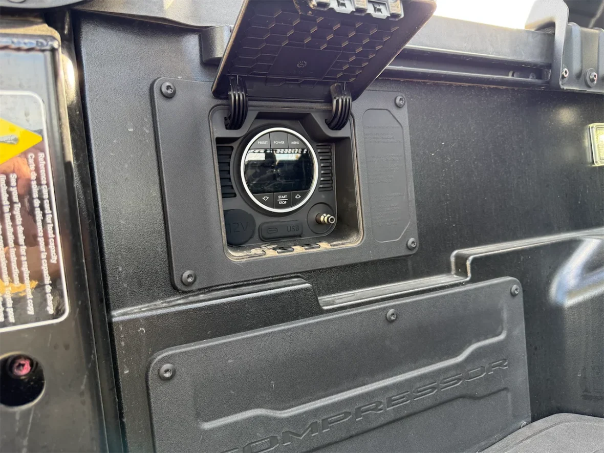 Close-up of a control panel featuring a round display with buttons, mounted in the interior of a vehicle.