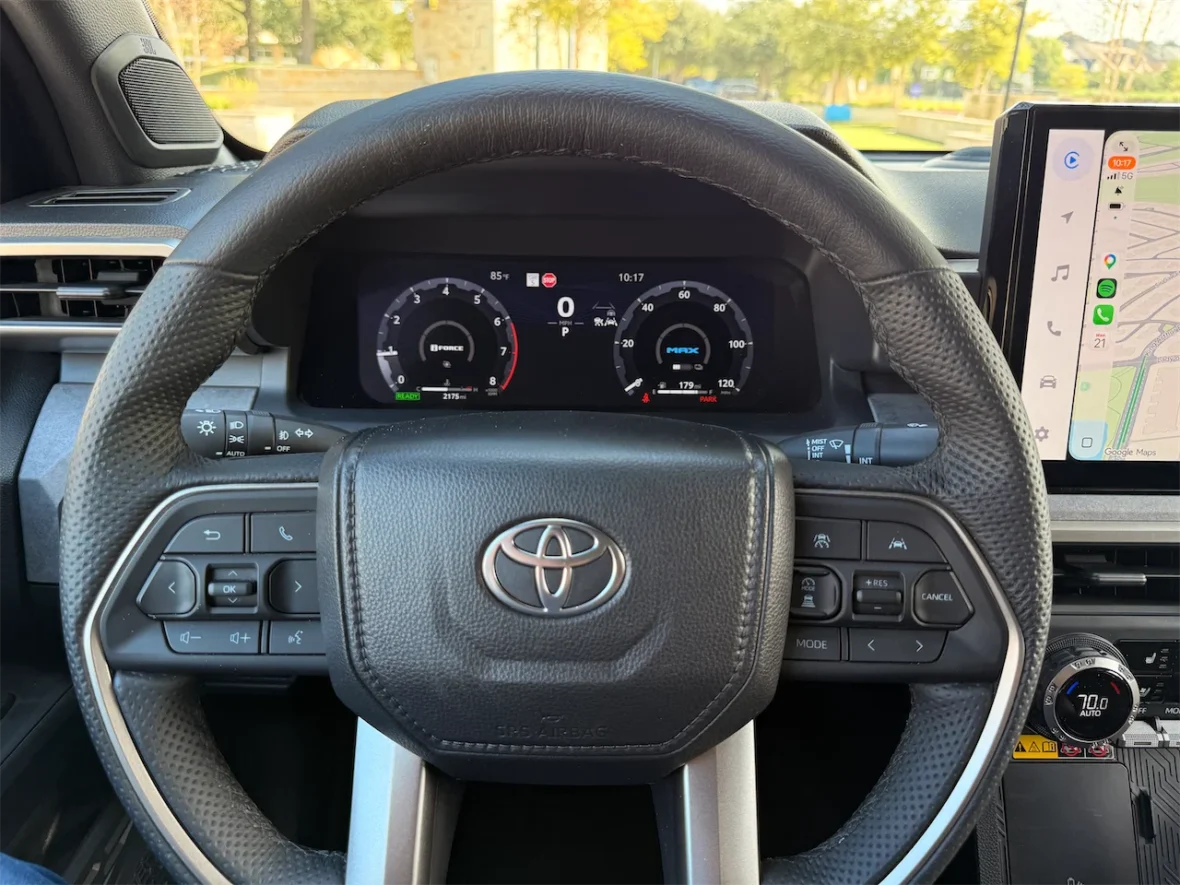 Interior view of a Toyota vehicle's steering wheel and dashboard, featuring digital gauges and a mounted touchscreen display with navigation.