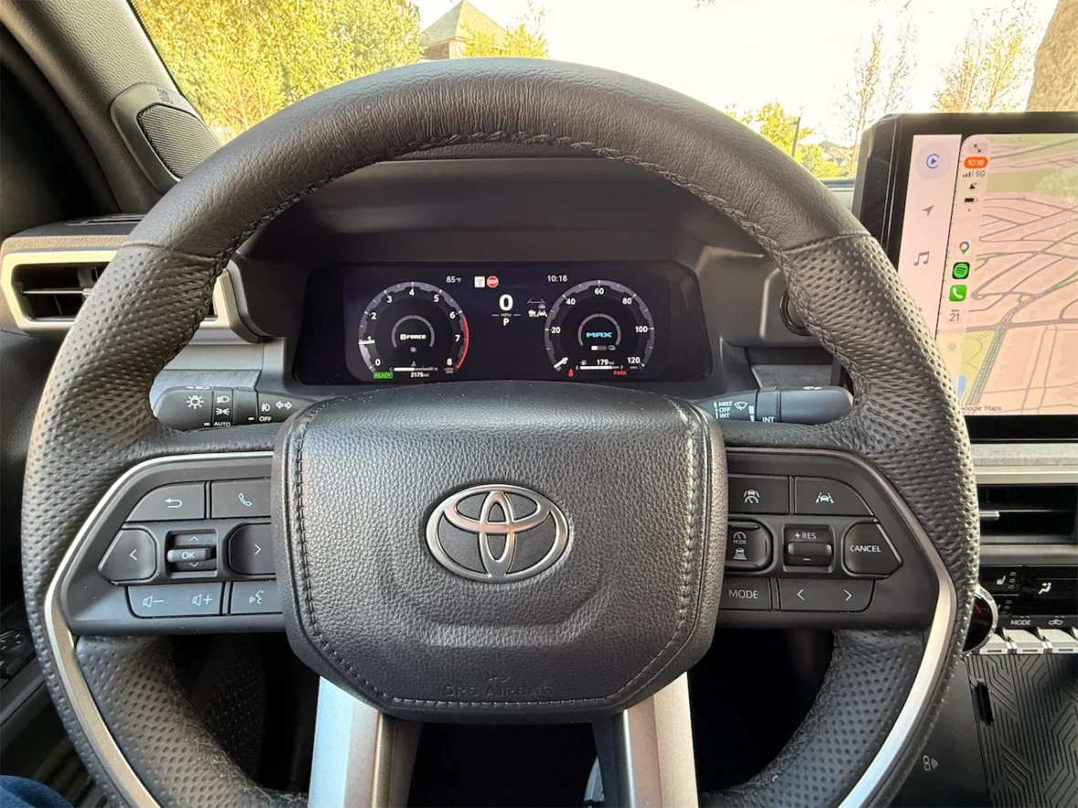 Dashboard view of a Toyota vehicle with a black steering wheel and control buttons, featuring digital gauges and a touchscreen infotainment system displaying a map.