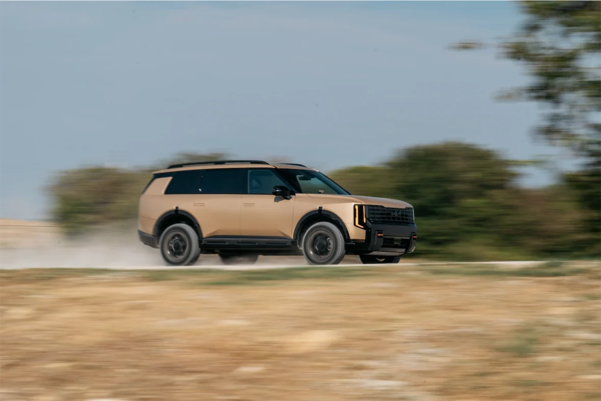 A rugged SUV driving on a dirt road, kicking up dust, surrounded by greenery in the background.