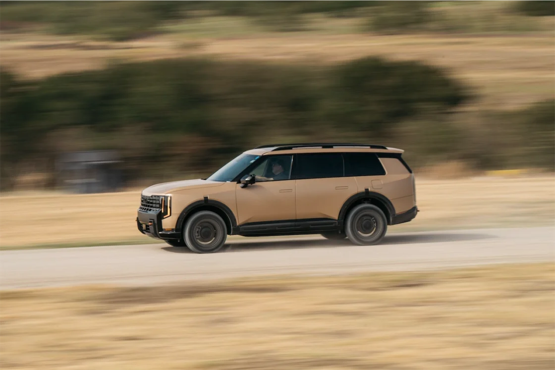 A beige SUV driving quickly on a gravel road with a blurred background, depicting motion.