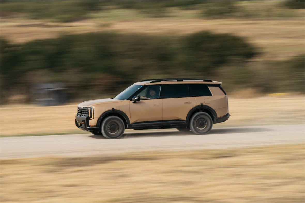 A beige SUV driving rapidly on a gravel road, set against a blurred backdrop of open fields.