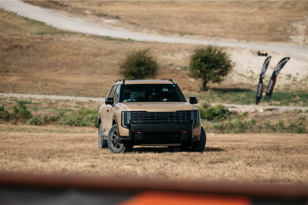 A tan SUV parked in an open grassy area with a dirt path in the background.