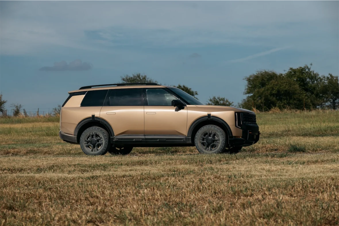 A side view of a golden SUV parked in a grassy field under a clear sky.