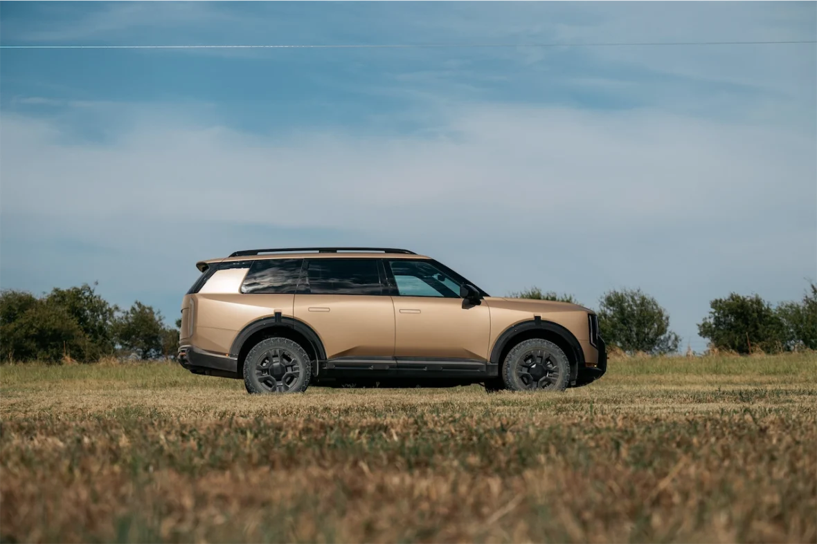 Side view of a modern, gold SUV parked on grassy terrain with a clear blue sky in the background.