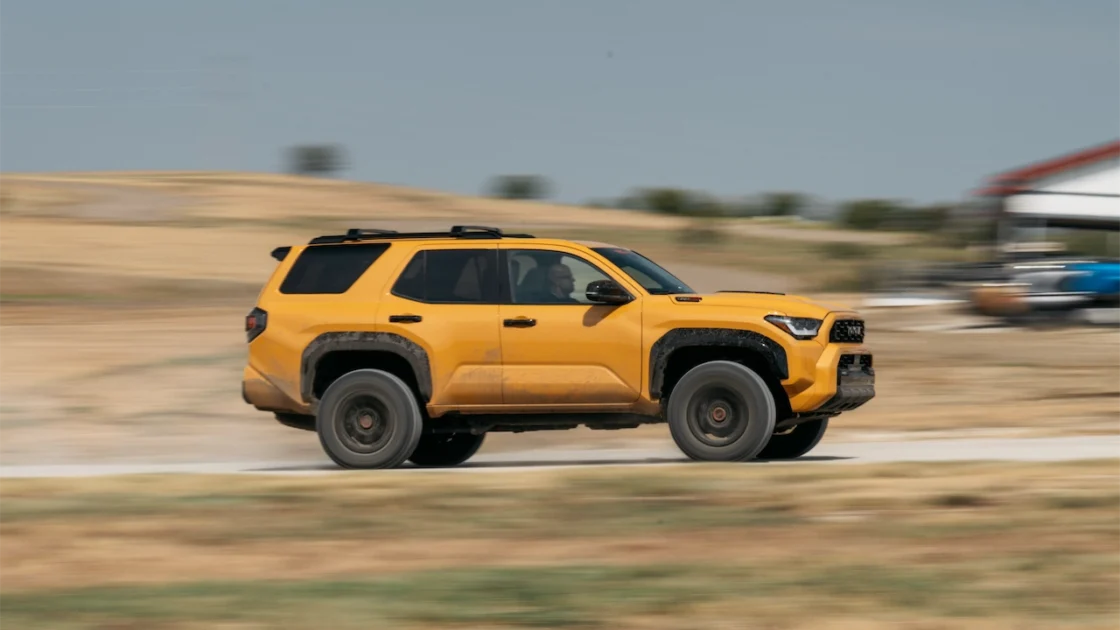 The 2027 Toyota 4Runner TRD Pro in Hot Honey driving past a field on a dirt road.