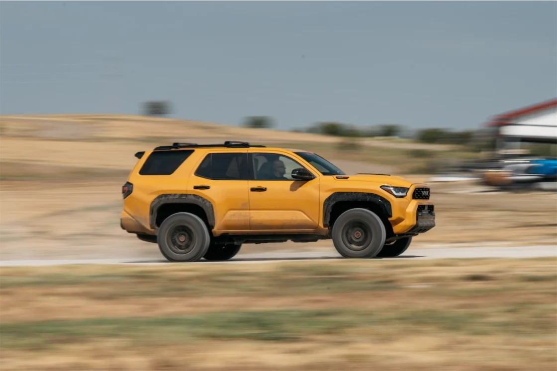 The 2027 Toyota 4Runner TRD Pro in Hot Honey driving past a field on a dirt road.