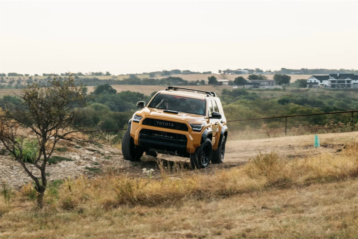 A yellow Toyota SUV driving off-road on a grassy terrain with hills in the background.