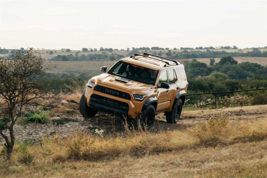 A yellow Toyota SUV flexing its suspension over uneven ground on an off-road course.