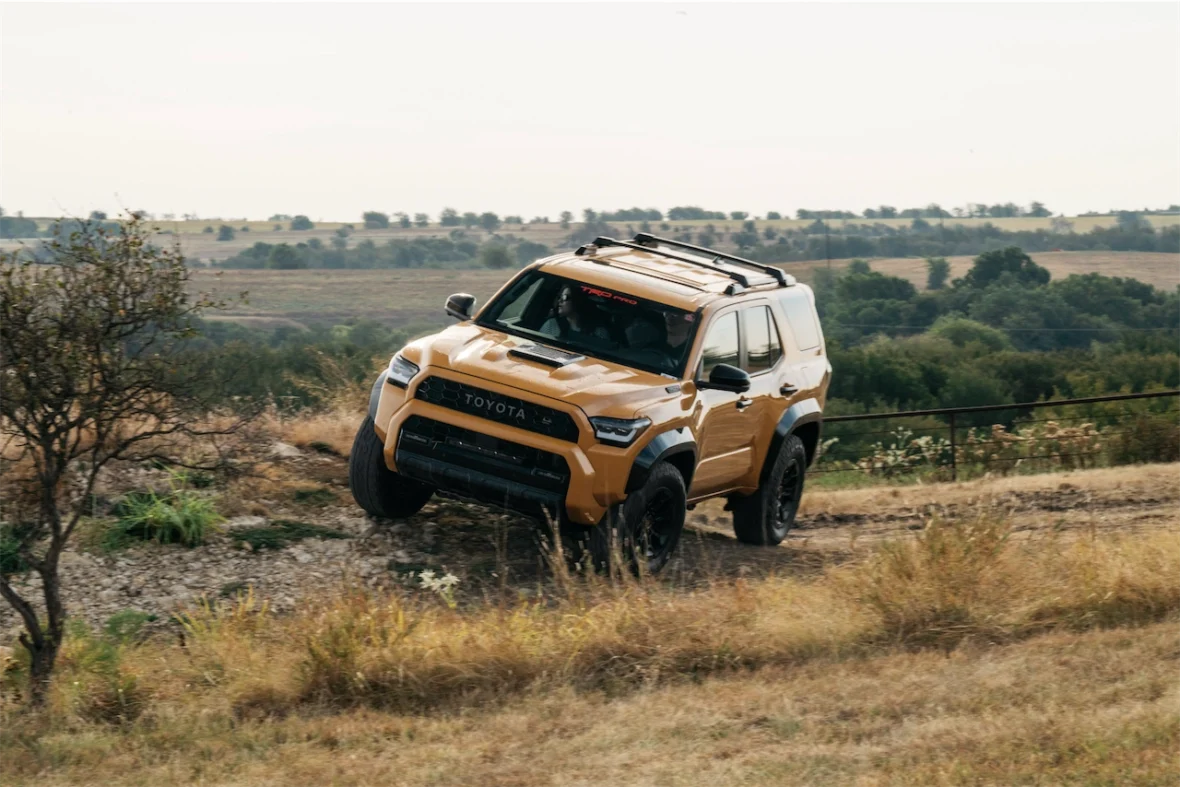 A yellow Toyota SUV driving on an uneven dirt terrain with one front wheel elevated.