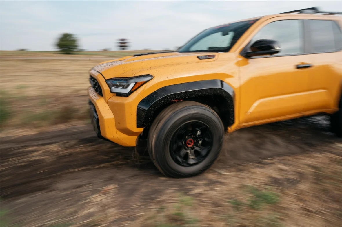 A bright yellow SUV driving through a muddy field, with the wheels in motion and dirt spraying up.