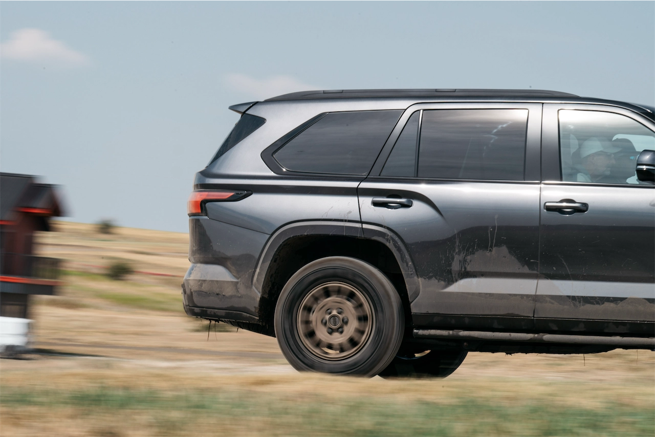 Side view of a gray three-row SUV in motion on a dirt course