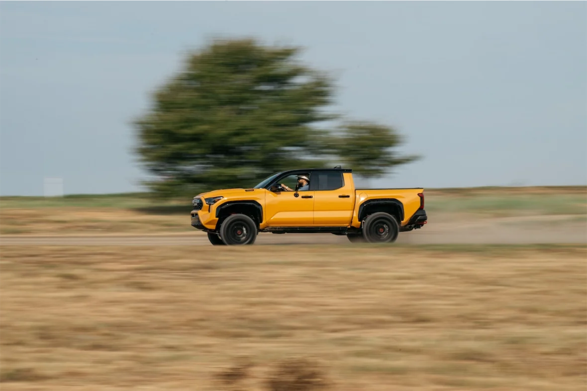 A bright yellow pickup truck speeding down a dirt road with a blurred background, suggesting motion.