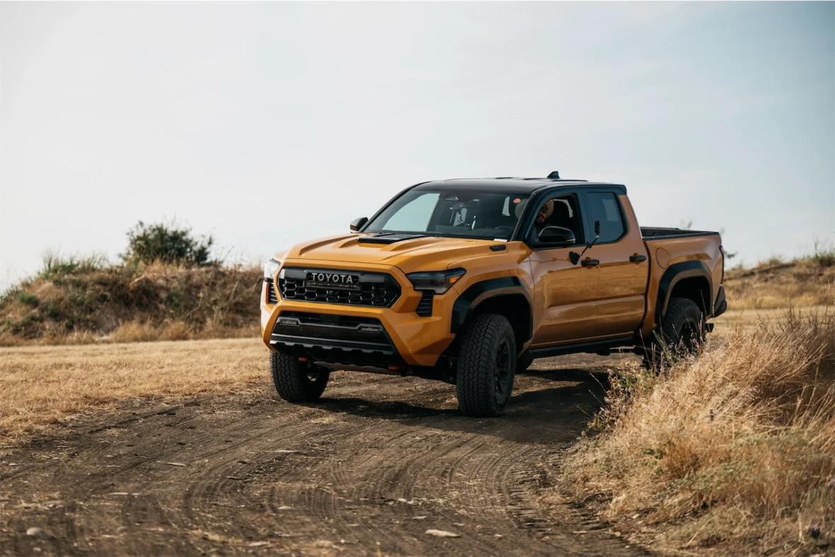 A yellow Toyota truck parked on a dirt road surrounded by dry grass and shrubs.