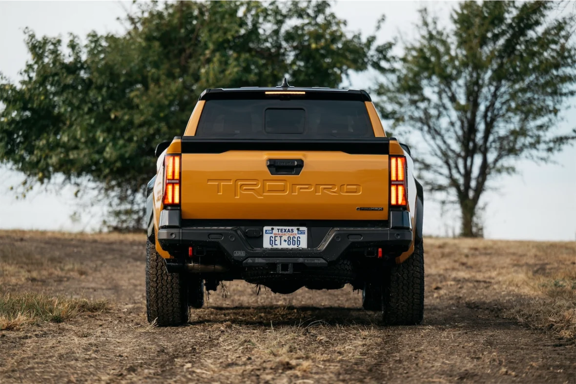 A rear view of a yellow truck parked on a gravel road, showcasing the TRD Pro logo and surrounding trees in the background.