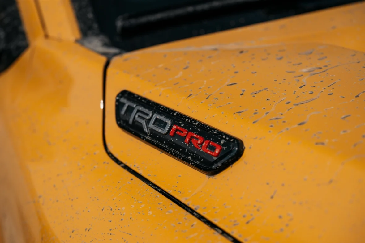 Close-up of a TRD Pro badge on a yellow vehicle with raindrops on the surface.
