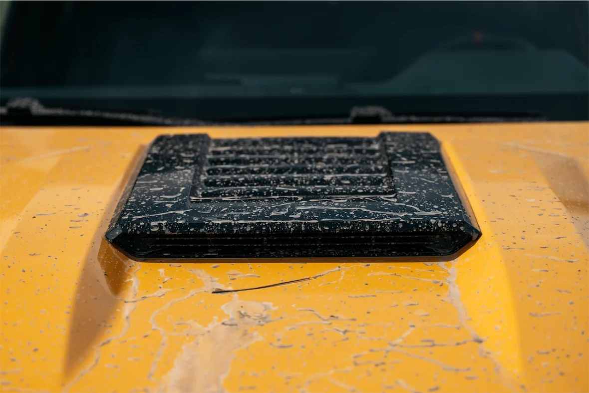 Close-up of a muddy hood scoop on a yellow vehicle, showcasing dirt and water splashes.