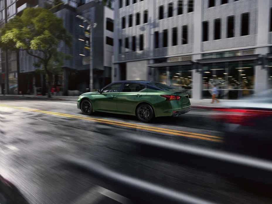 Rear three-quarter view of the midsize sedan driving along a city street, shown in 2026 form